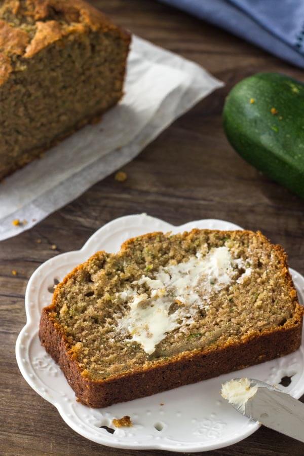 A slice of zucchini banana bread slathered with butter on a white plate. 