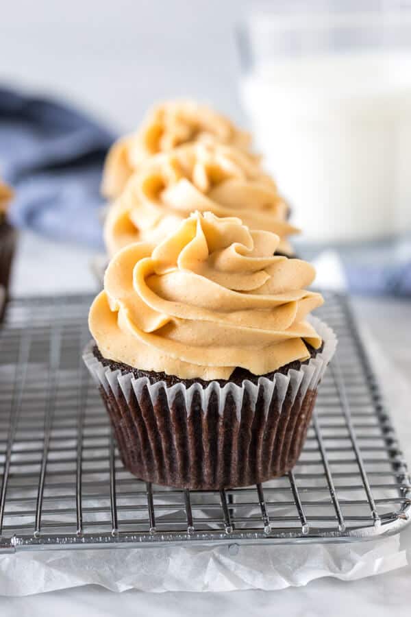 Chocolate cupcakes with peanut butter frosting on cooling rack with glass of milk.