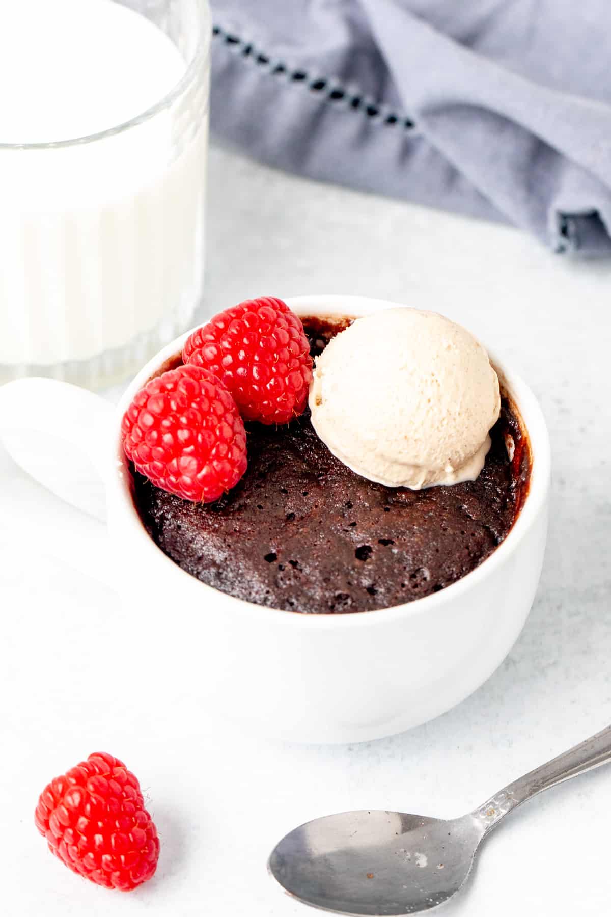 Individual chocolate mug cake with scoop of ice cream and 2 raspberries on top with glass of milk