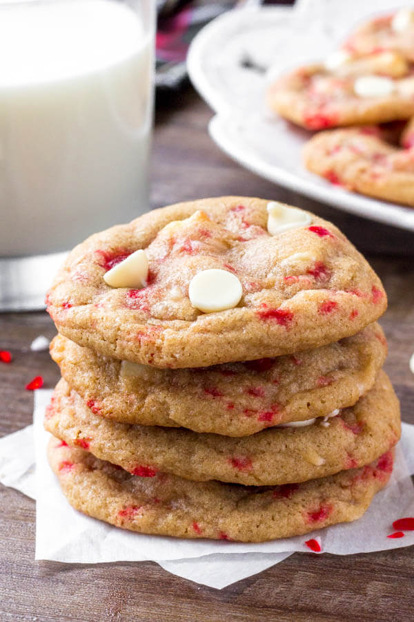 A stack of candy cane white chocolate cookies with a glass of milk. 