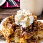 A slice of eggnog French toast bake with crumb topping, maple syrup and whipped cream.