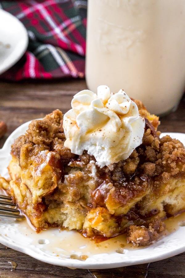 A slice of eggnog French toast bake with crumb topping, maple syrup and whipped cream. 