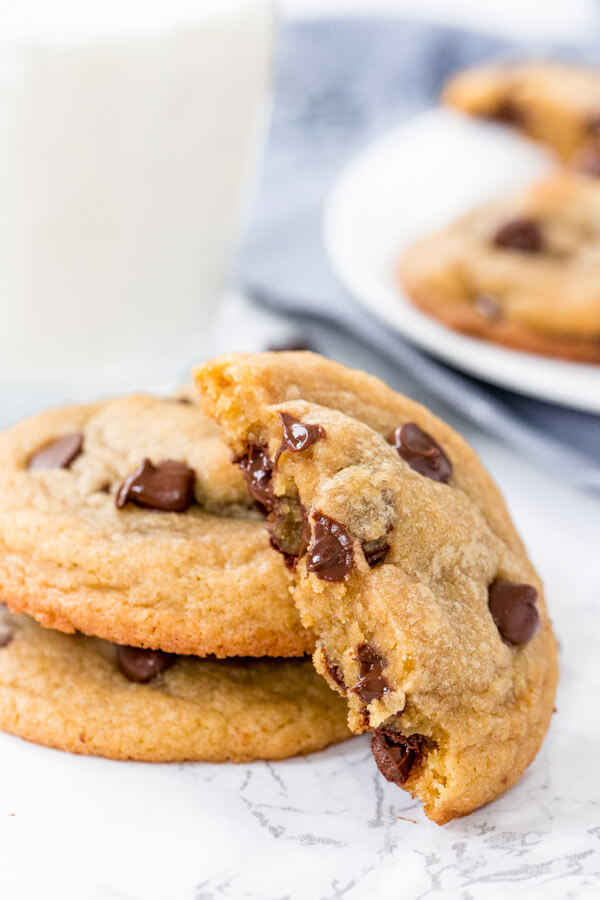 A stack of chocolate chip cookies with one cookie broken in half on it's side and a glass of milk. 