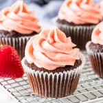 Chocolate cupcakes with strawberry frosting on cooling rack.