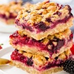 3 berry crumble bars made with oatmeal and brown sugar stacked on a white plate.