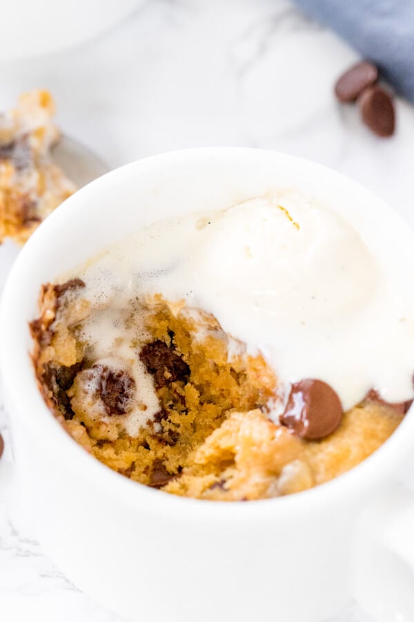 Overhead shot of a chocolate chip cookie in a mug with vanilla ice cream and a bite taken out of it. 