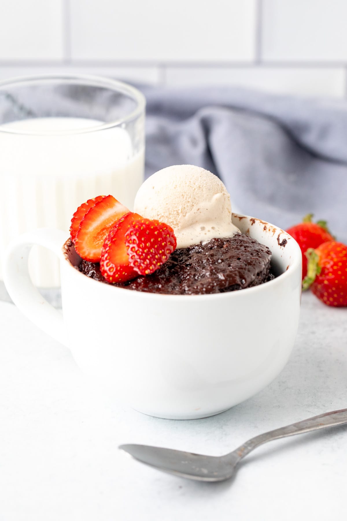 Single serving Nutella cake in a mug, topped with ice cream and berries with glass of milk