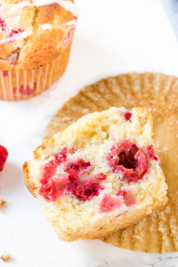 A moist, fluffy raspberry muffin broken in half to show the berries in side. 
