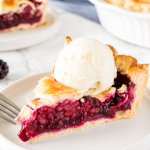 A slice of blackberry pie with flaky pastry and a scoop of vanilla ice cream on top.