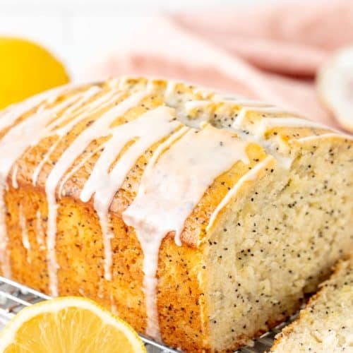 Half of a lemon poppy seed loaf drizzled with lemon glaze on a cooling rack