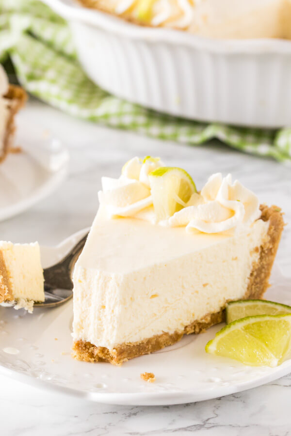 A slice of key lime pie on a white plate with a bite taken out of it to show the creamy, smooth texture.