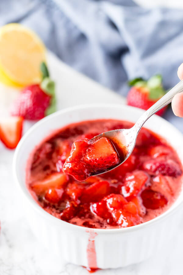 A dish filled with strawberry sauce to serve on cheesecake, pancakes or ice cream. A spoon serving the sauce to show the juicy strawberry pieces.