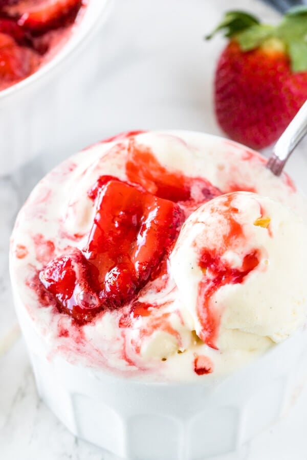 A bowl of ice cream with strawberry sundae sauce with thick, juicy pieces of berries and the ice cream starting to melt.