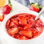 A white dish of strawberry sauce with strawberries in the background.