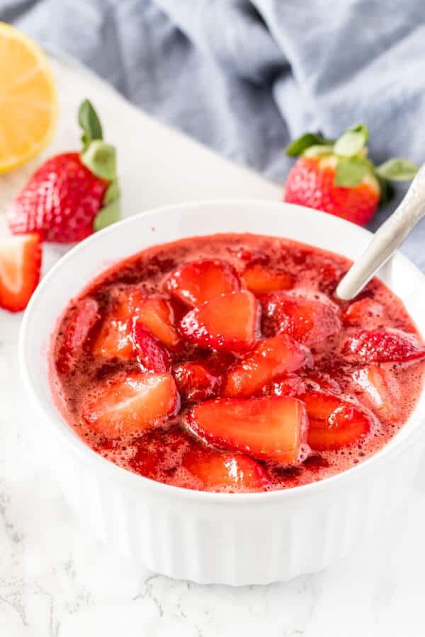 A white dish of strawberry sauce with strawberries in the background.