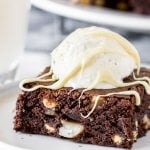A fudgy white chocolate macadamia nut brownie on a white plate with a scoop of vanilla ice cream to make a brownie sundae.