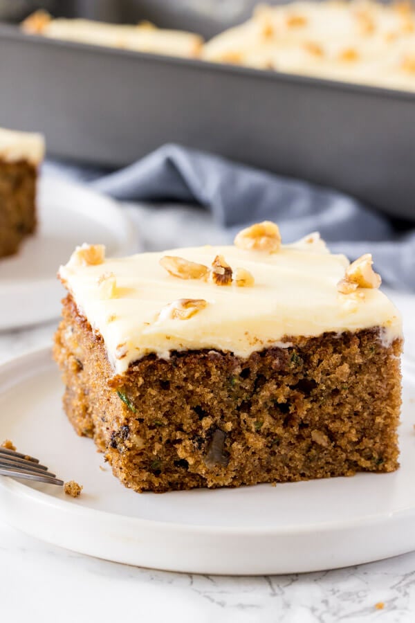 A side angle shot of moist, tender zucchini cake with cream cheese frosting and topped with a few chopped walnuts. 