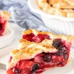 A slice of mixed berry pie with strawberries, blueberries and raspberries in the filling with a flaky lattice top crust.