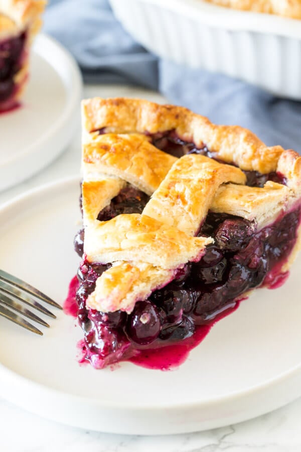 A slice of homemade blueberry pie with a juicy fruit filling and flaky lattice crust on top.