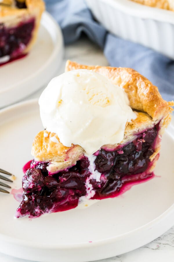 A slice of homemade blueberry pie with flaky crust and topped with a scoop of ice creamy. 