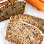 Close up of 3 slices of banana carrot bread with the rest of the loaf and 2 carrots to show the moist crumb.