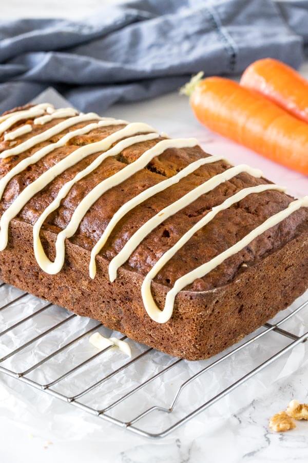 Carrot banana bread with a drizzle of cream cheese glaze pictured as the whole loaf on a wire cooling rack. 