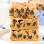 A stack of 3 chewy chocolate chip cookie bars with a glass of milk.