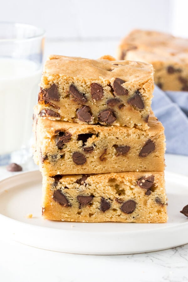 A stack of 3 chewy chocolate chip cookie bars with a glass of milk. 
