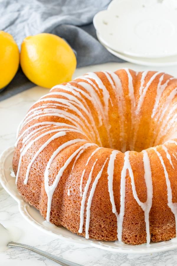 Moist lemon bundt cake with a drizzle of lemon glaze on a white plate.