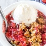 A bowl of strawberry rhubarb crisp with a juicy fruit filling and oatmeal brown sugar crumble on top. Served with a scoop of vanilla ice cream