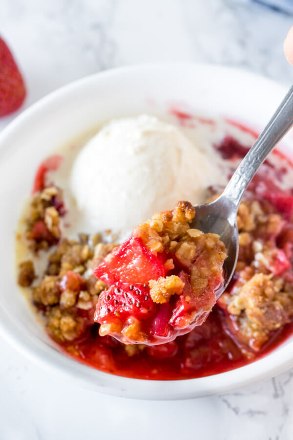 Close up of a spoonful of strawberry rhubarb crisp with juicy pieces of fruit and oatmeal crumble. 