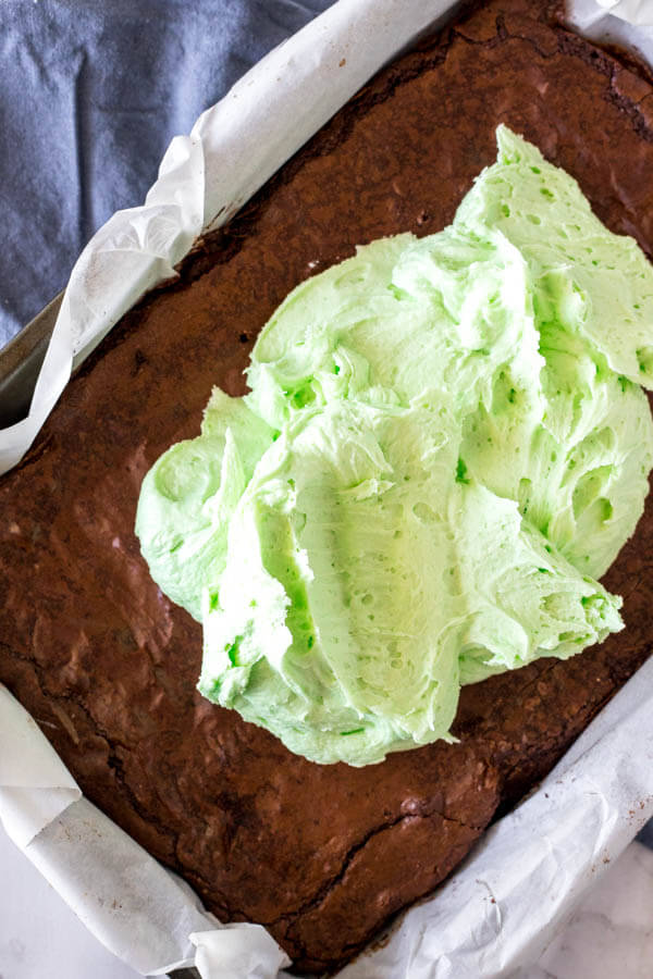 Mint frosting being spread on top of the brownie layer when making mint chocolate brownies. 