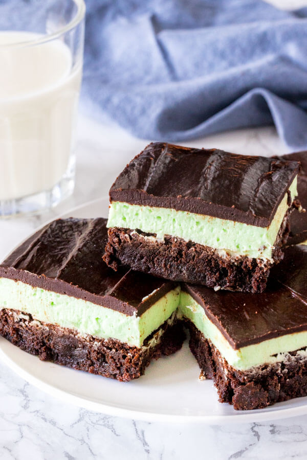 A plate of mint brownies with a fudgy brownie base, mint frosting middle, and chocolate ganache on top. 
