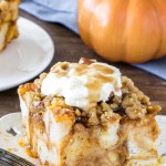 A slice of pumpkin French toast casserole with streusel topping with whipped cream and maple syrup to serve