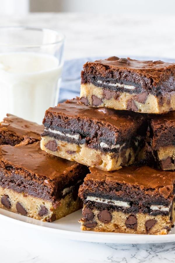 A plate of slutty brownies cut into squares and stacked to show the brownie base, oreos in the middle, and brownie layer on top. 