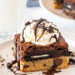 A cookie dough oreo brownie with a scoop of ice cream, chocolate sauce and oreo crumbs on top.