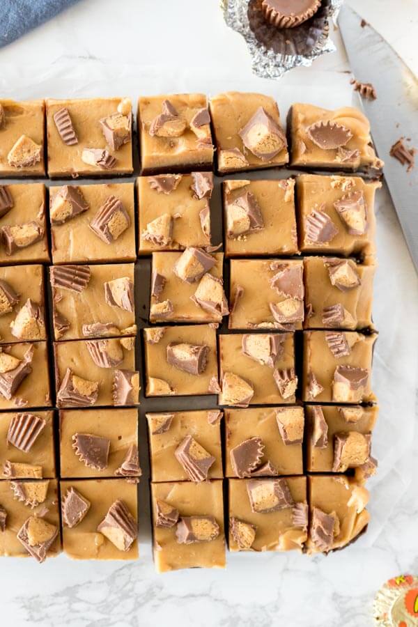 A pan of chocolate peanut butter fudge with peanut butter cups on top cut into pieces and photographed from above.