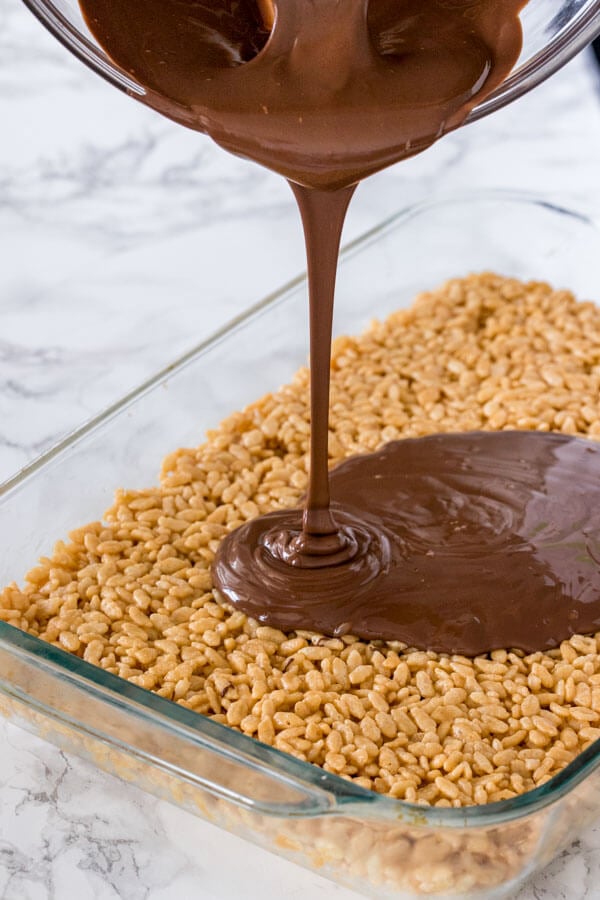 Pouring the chocolate topping over a pan of peanut butter rice krispie treats.