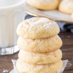 A stack of 4 cream cheese cookies taken from the side with a glass of milk.