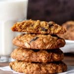 Thick and chewy oatmeal raisin cookies stacked on top of each other, with top cookie broken in half.