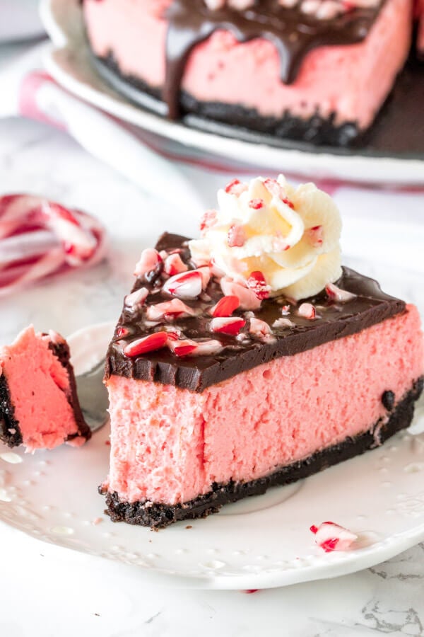 A piece of candy cane cheesecake with a bite taken out on a white plate.