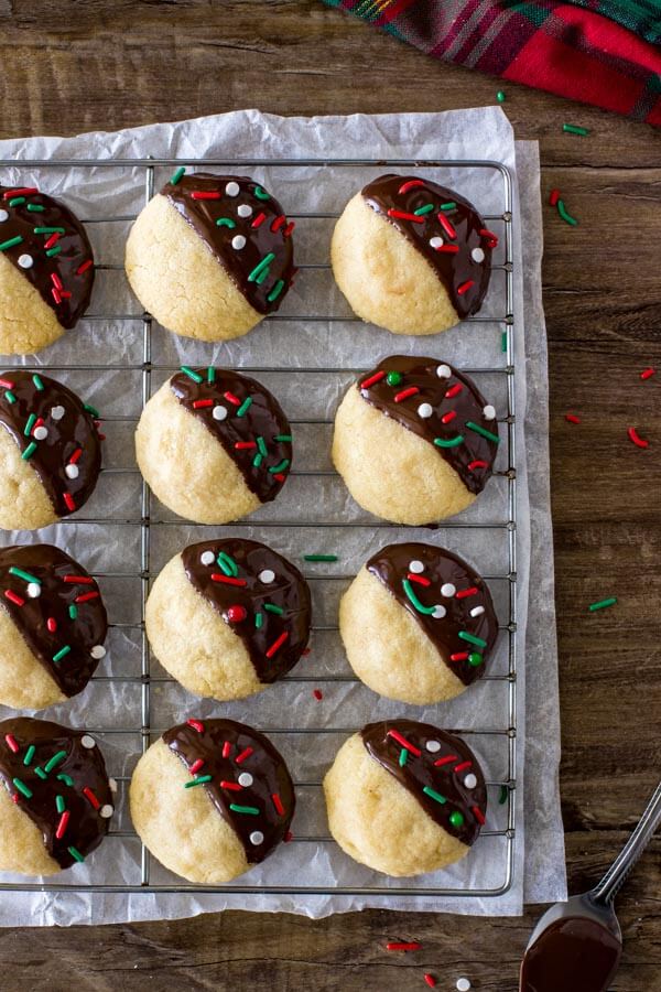 A wire cooling rack of shortbread cookie balls with each cookie dipped half in chocolate.
