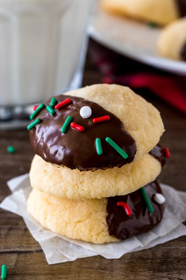 A stack of 3 chocolate dipped shortbread cookies with a glass of milk