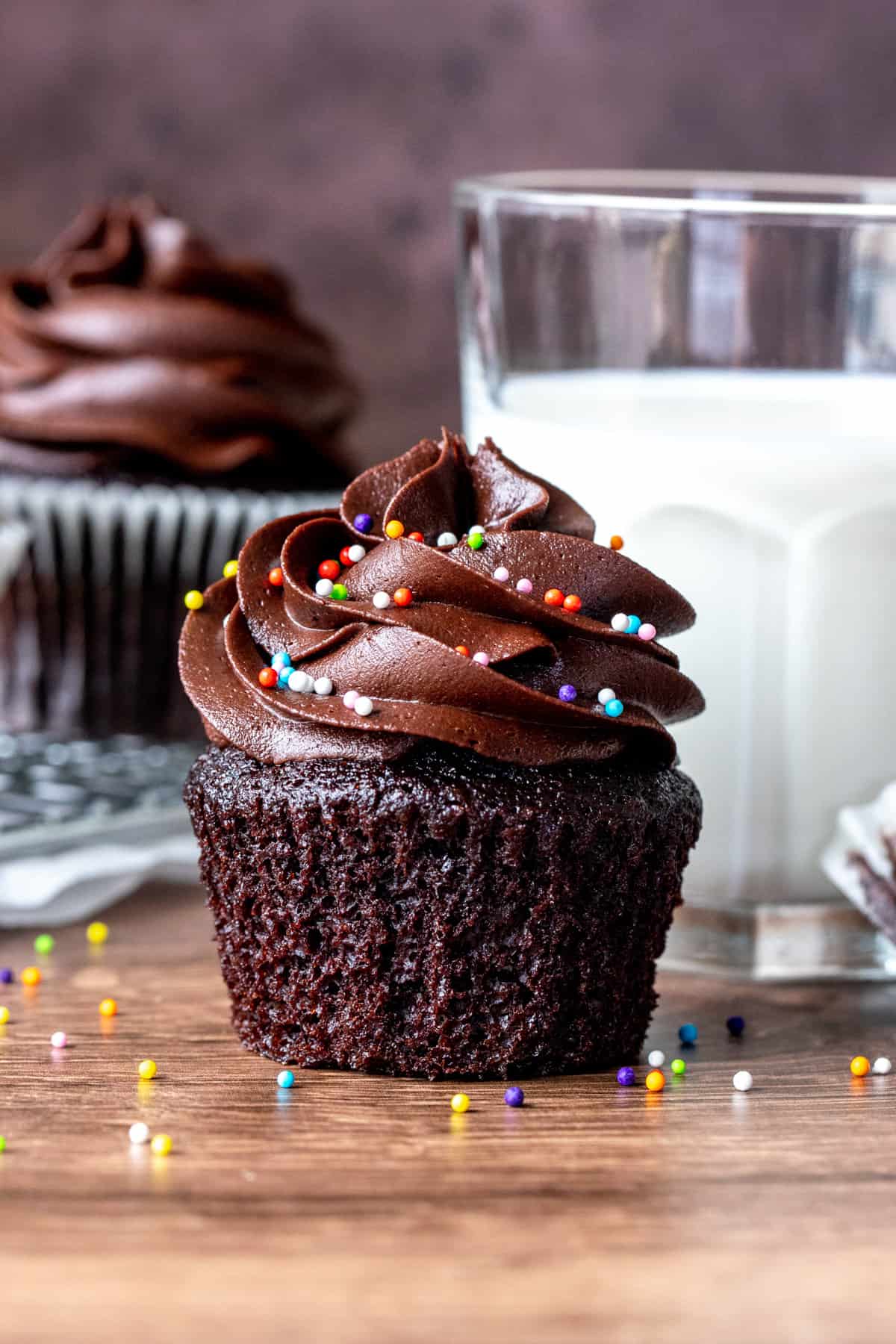 Chocolate cupcake with paper removed beside glass of milk