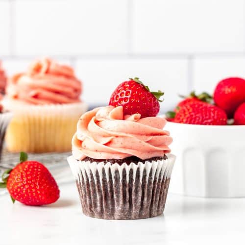 Chocolate cupcake decorated with strawberry buttercream frosting and topped with a berry