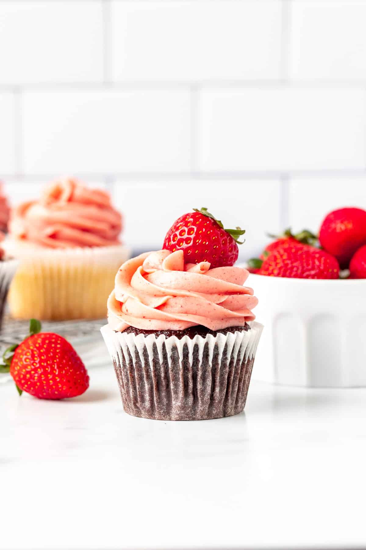 Chocolate cupcake decorated with strawberry buttercream frosting and topped with a berry