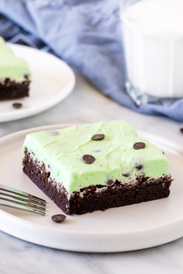 Brownie topped with mint chip frosting on a plate with a glass of milk