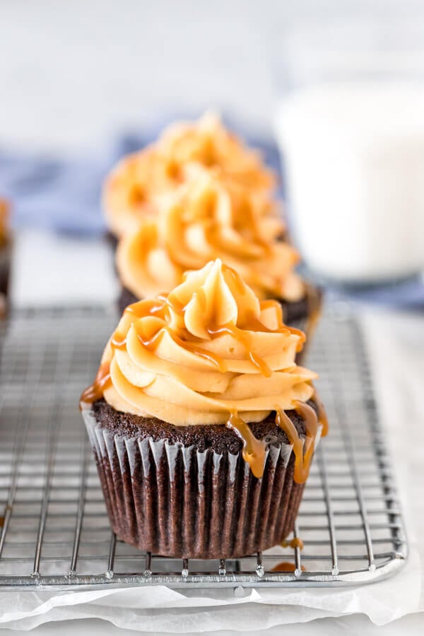 Chocolate cupcakes with caramel frosting drizzled with caramel sauce on a wire rack. 