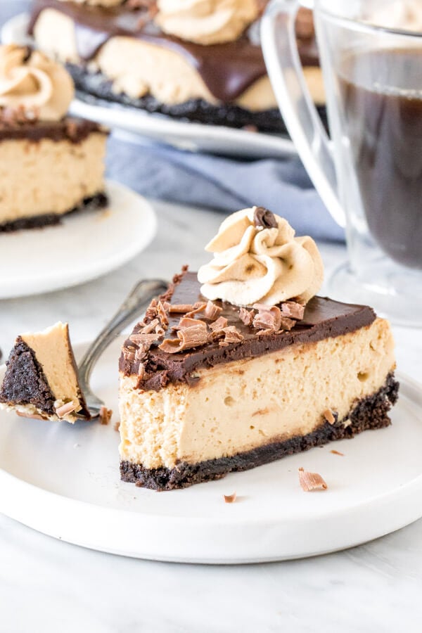 Slice of coffee cheesecake with chocolate ganache on top on a plate with a bite taken out of it. 