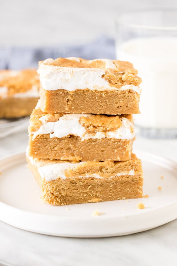 Stack of 3 marshmallow peanut butter bars on a plate with a glass of milk. 